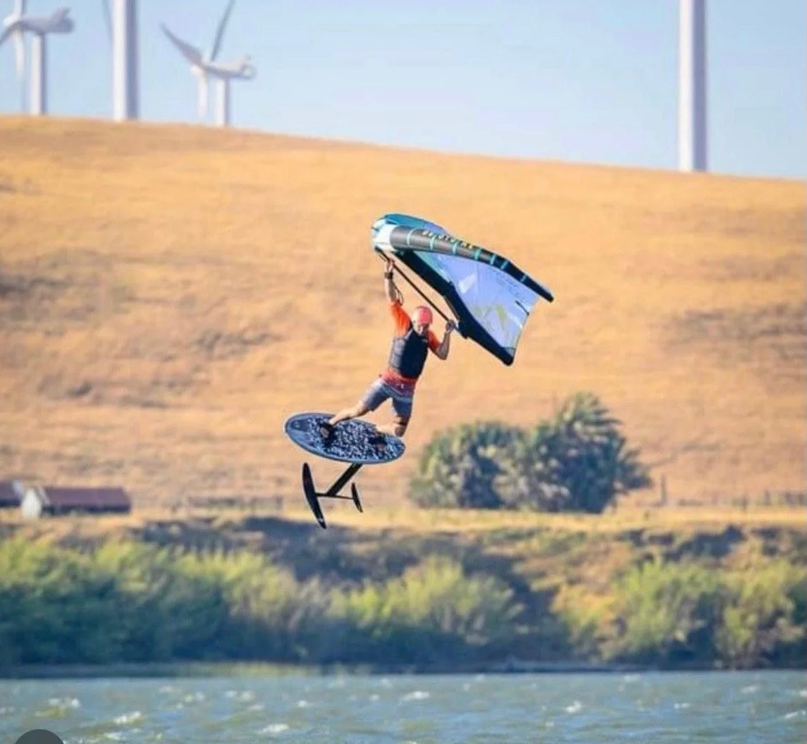 Wing foiling on a Vince Broglio board with wind turbines in background
