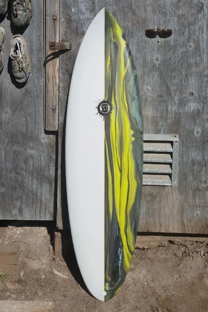 Custom handcrafted surfboard by Vince Broglio leaning against a weathered wooden wall